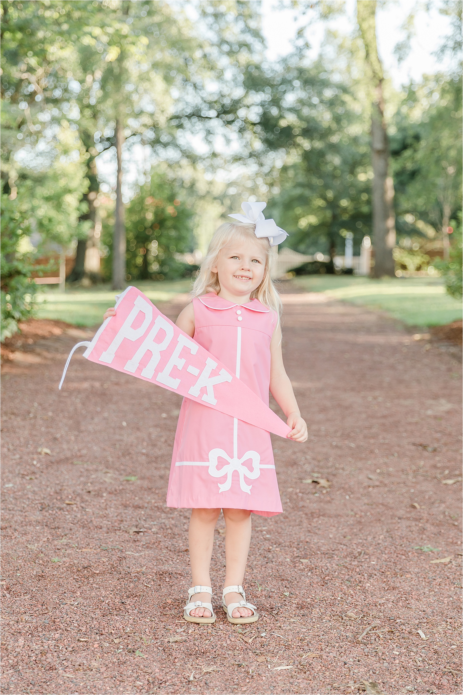 Young girl in pink Beaufort Bonnet Dress holding a Pre-K banner
