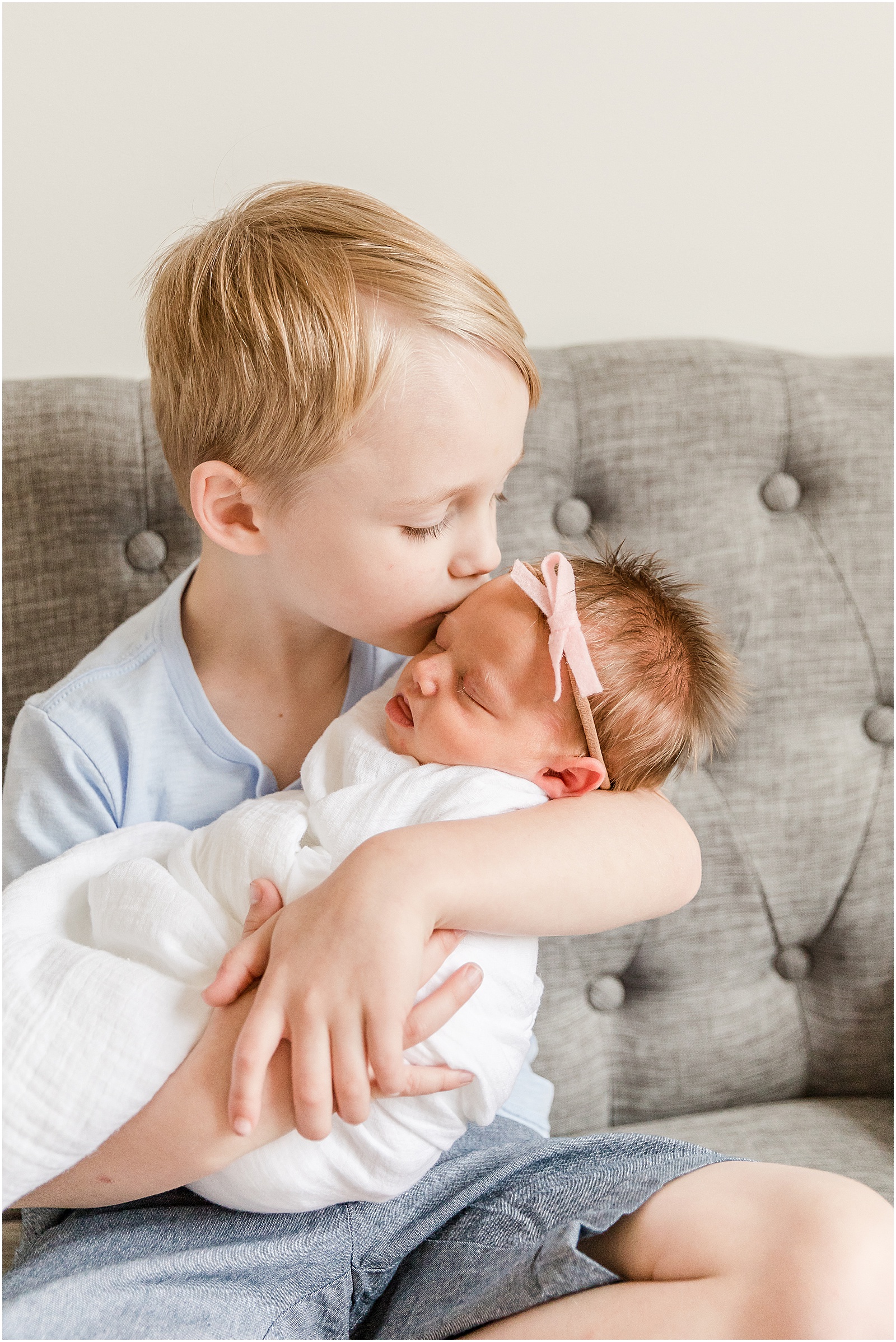 Young boy holding his newborn baby sister and kissing her forehead
