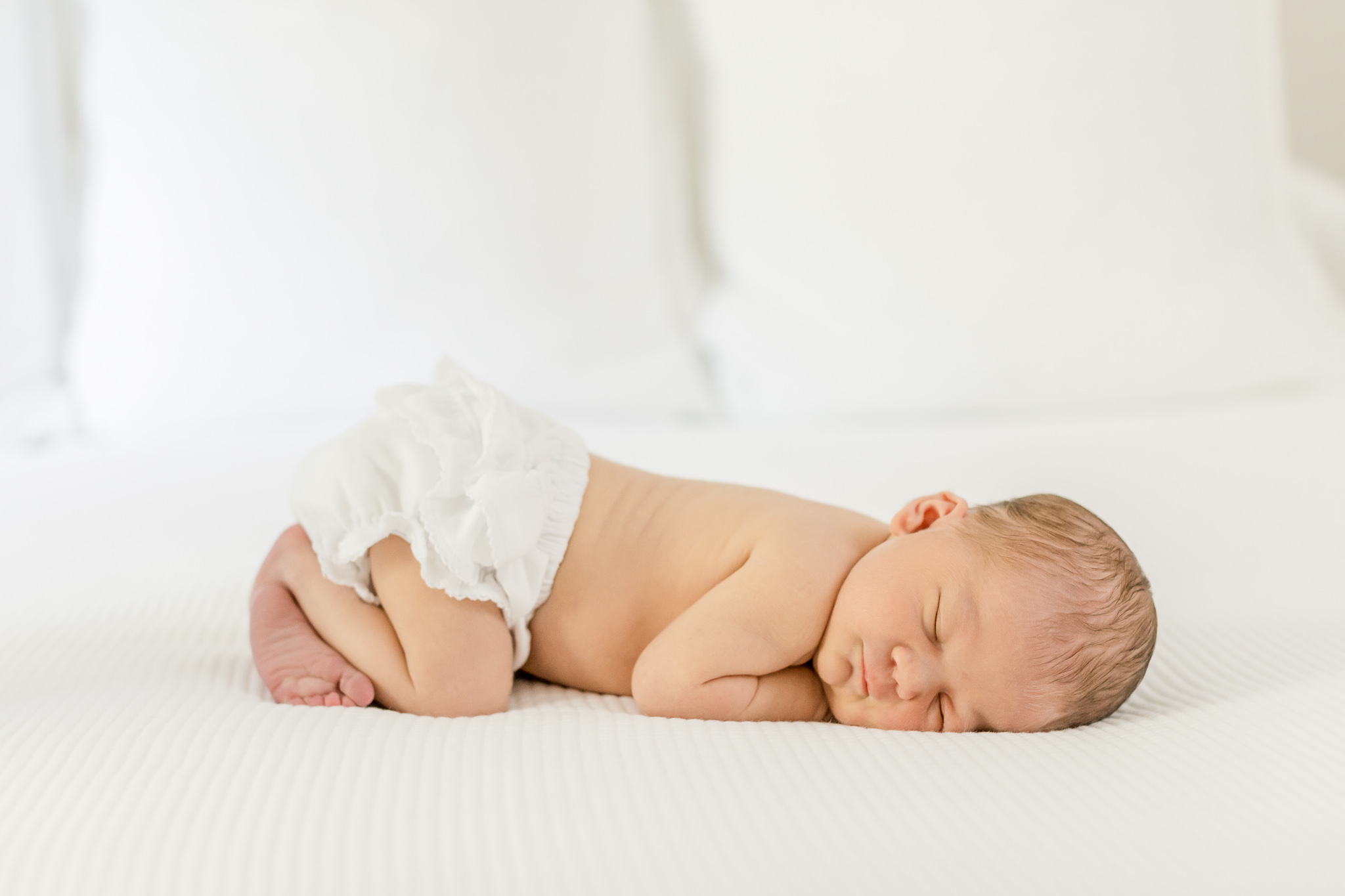 A baby in bloomers snuggled up on a white comforter by Greenville SC newborn photographer Molly Hensley.
