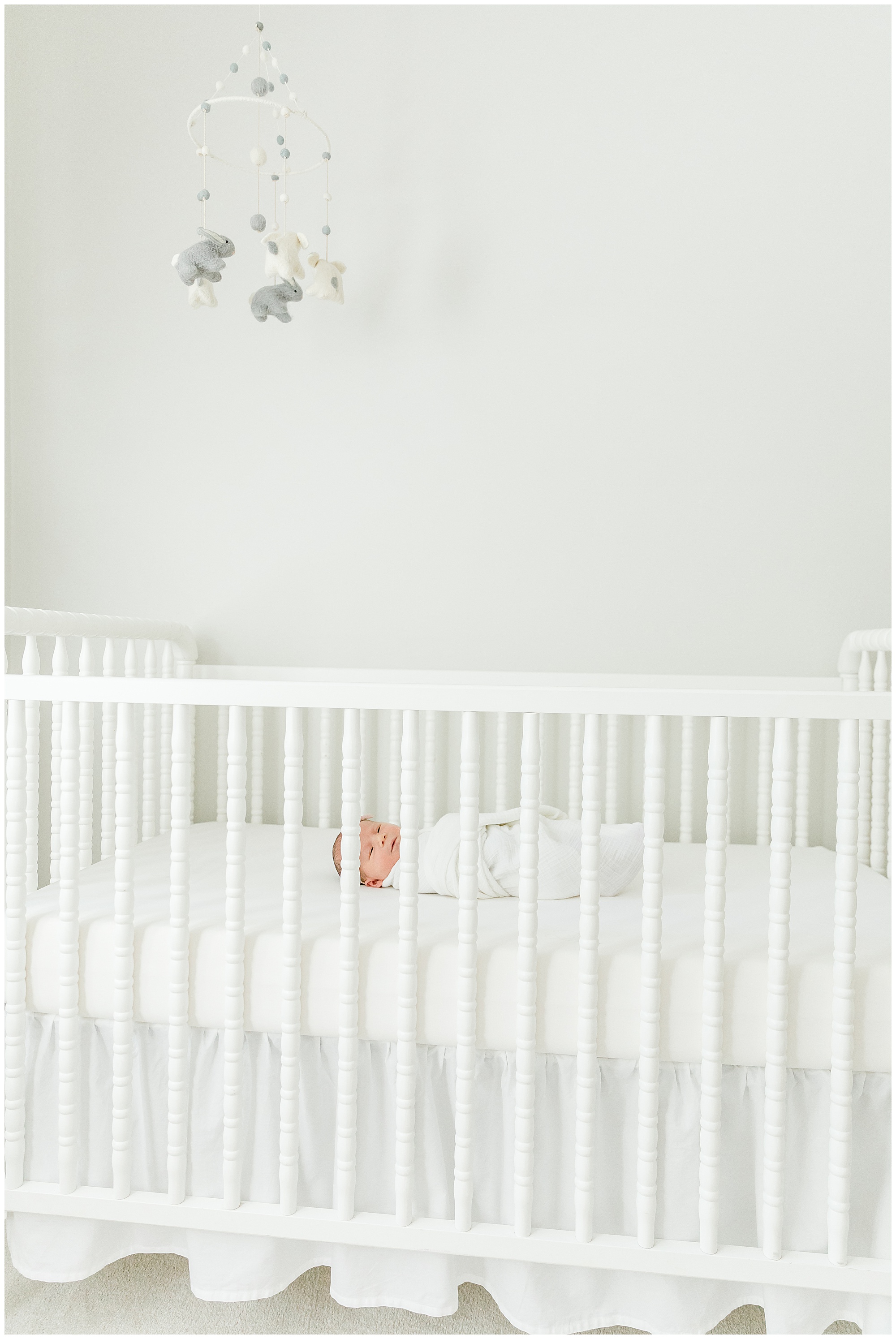 baby girl in a white crib with a gray and white mobile