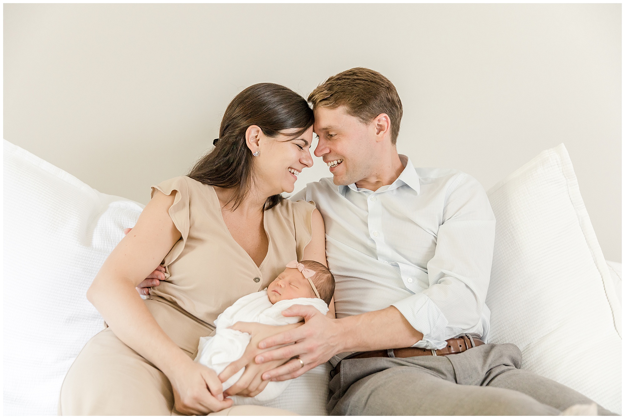 Mother and father smiling at one another with foreheads touching while holding baby girl for greenville newborn photos