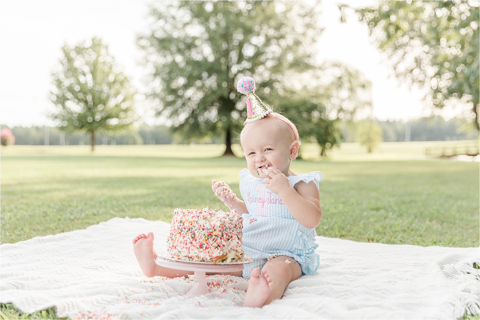 Baby girl with party hat eating sprinkle cake by photographer in Greenville SC