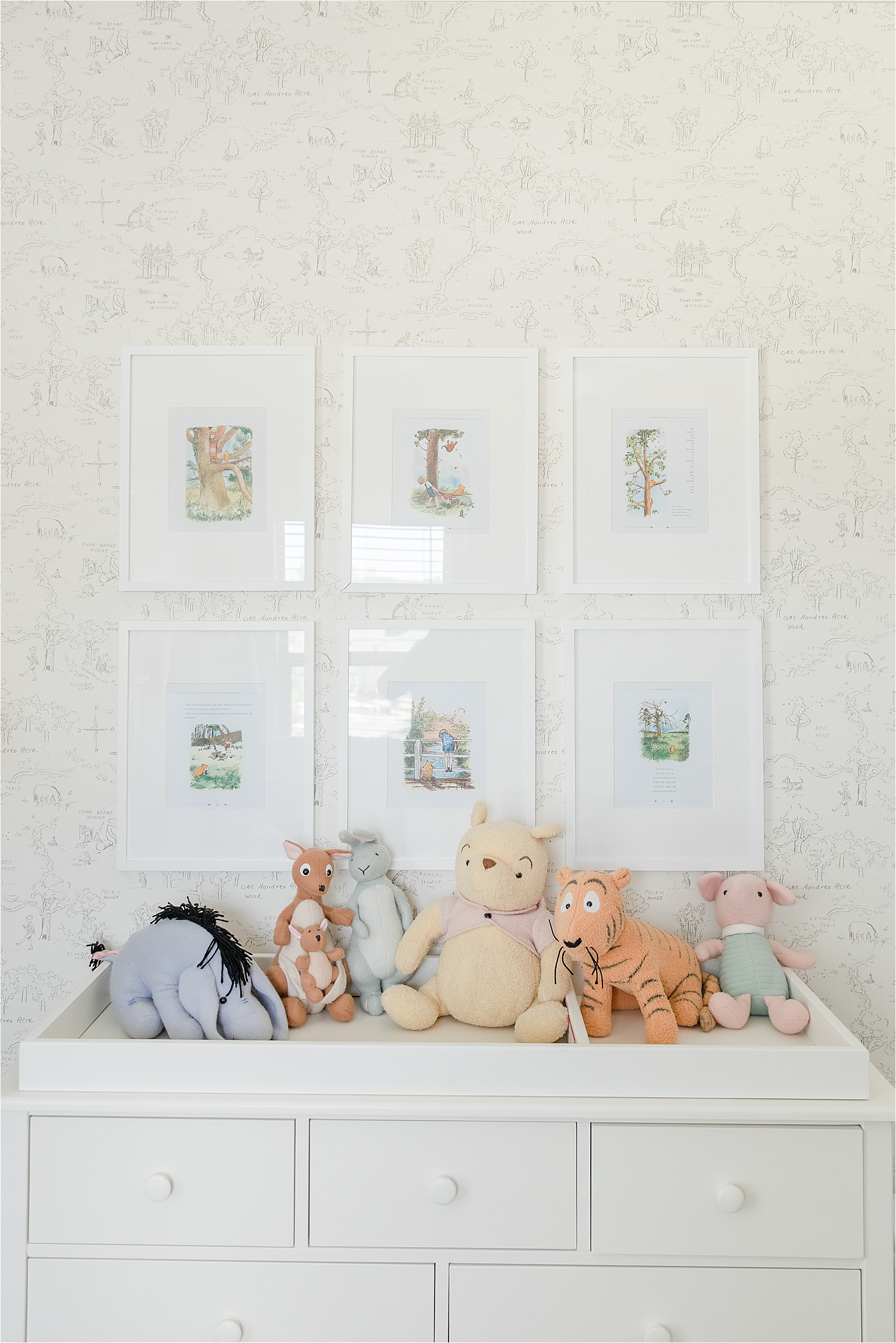 Framed pages from Winnie the Pooh book above changing table in nursery with vintage stuffed characters