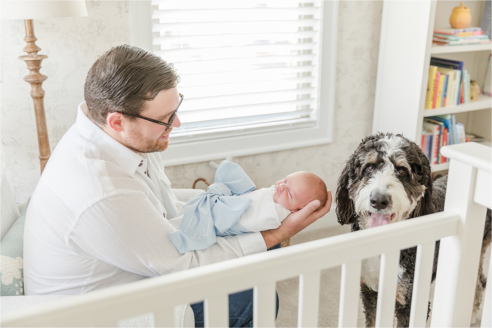 Dad holding baby in Beaufort Bonnet Bow Swaddle as Dog looks at camera