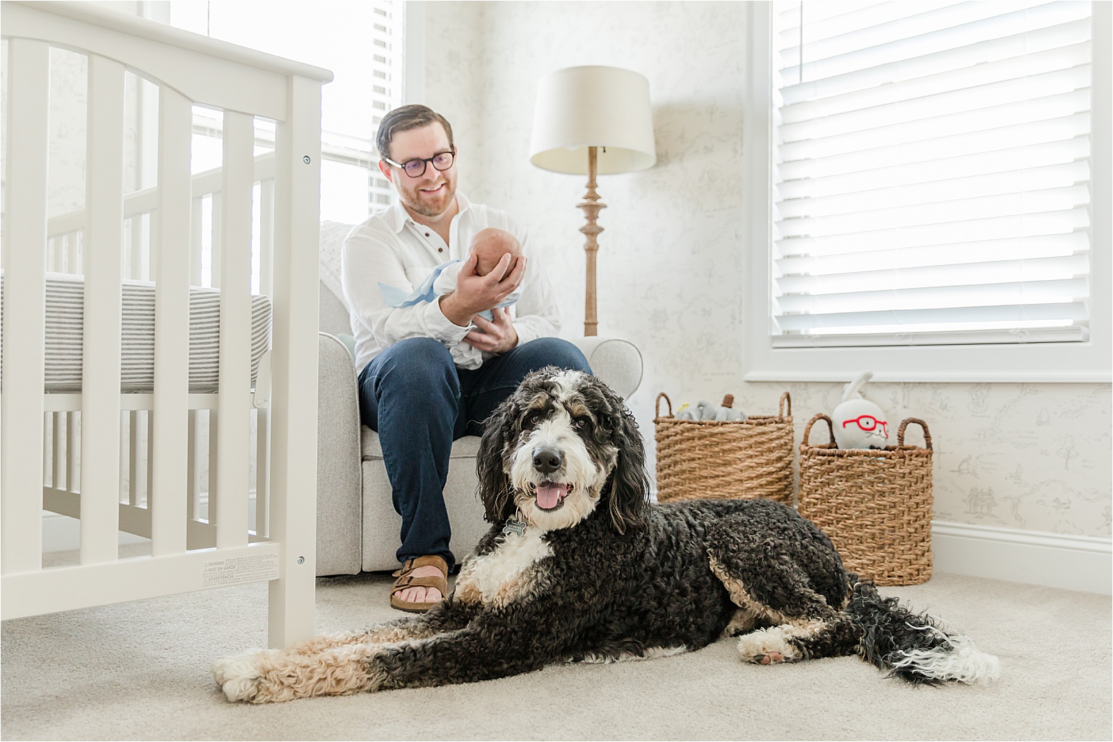 Father holding newborn son with large dog laying at his feet