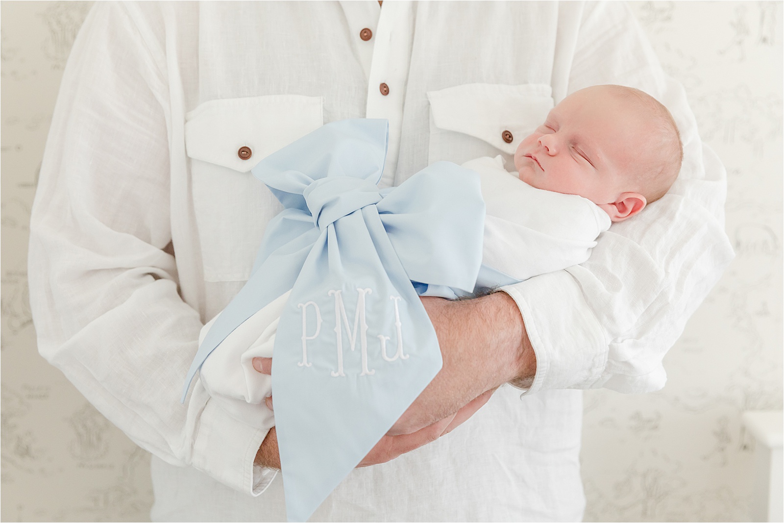 Baby boy wearing a Beaufort Bonnet Bow Swaddle in his fathers arms in a Greenville photography session in his Winnie the Pooh Nursery.