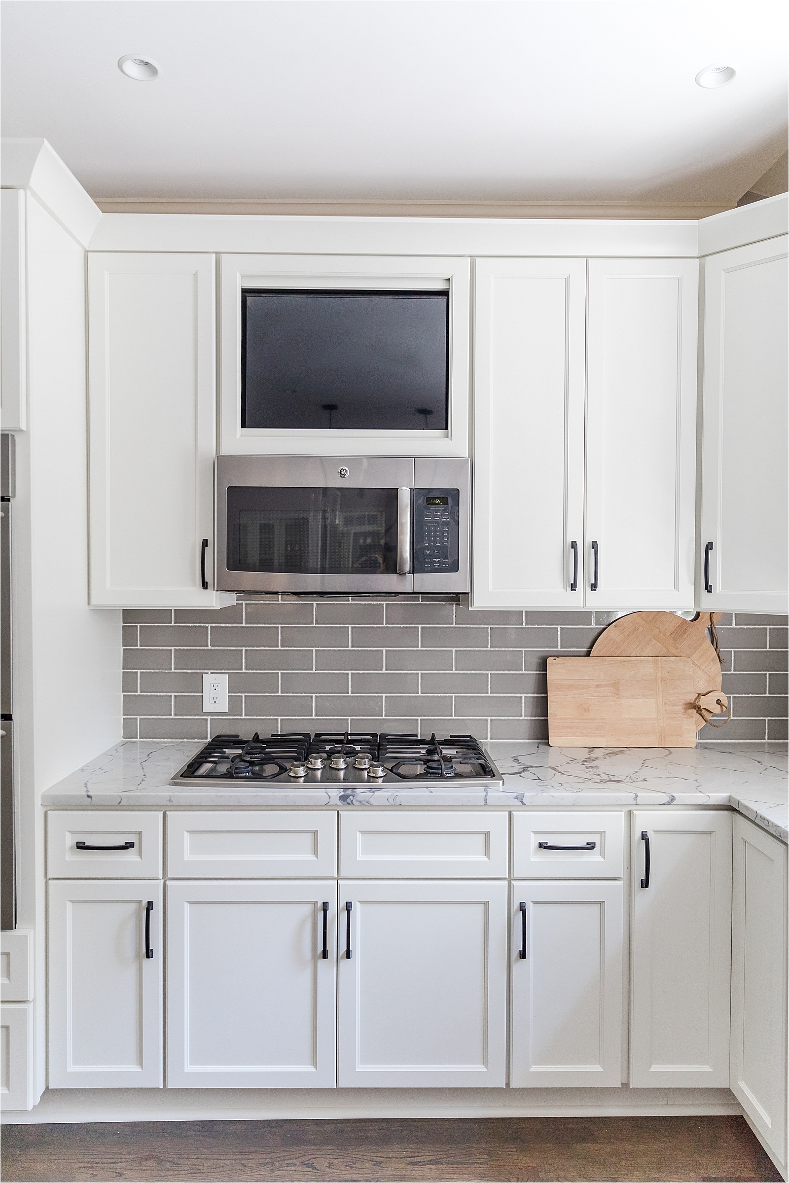 White cabinets, grey backsplash with built in tv about microwave