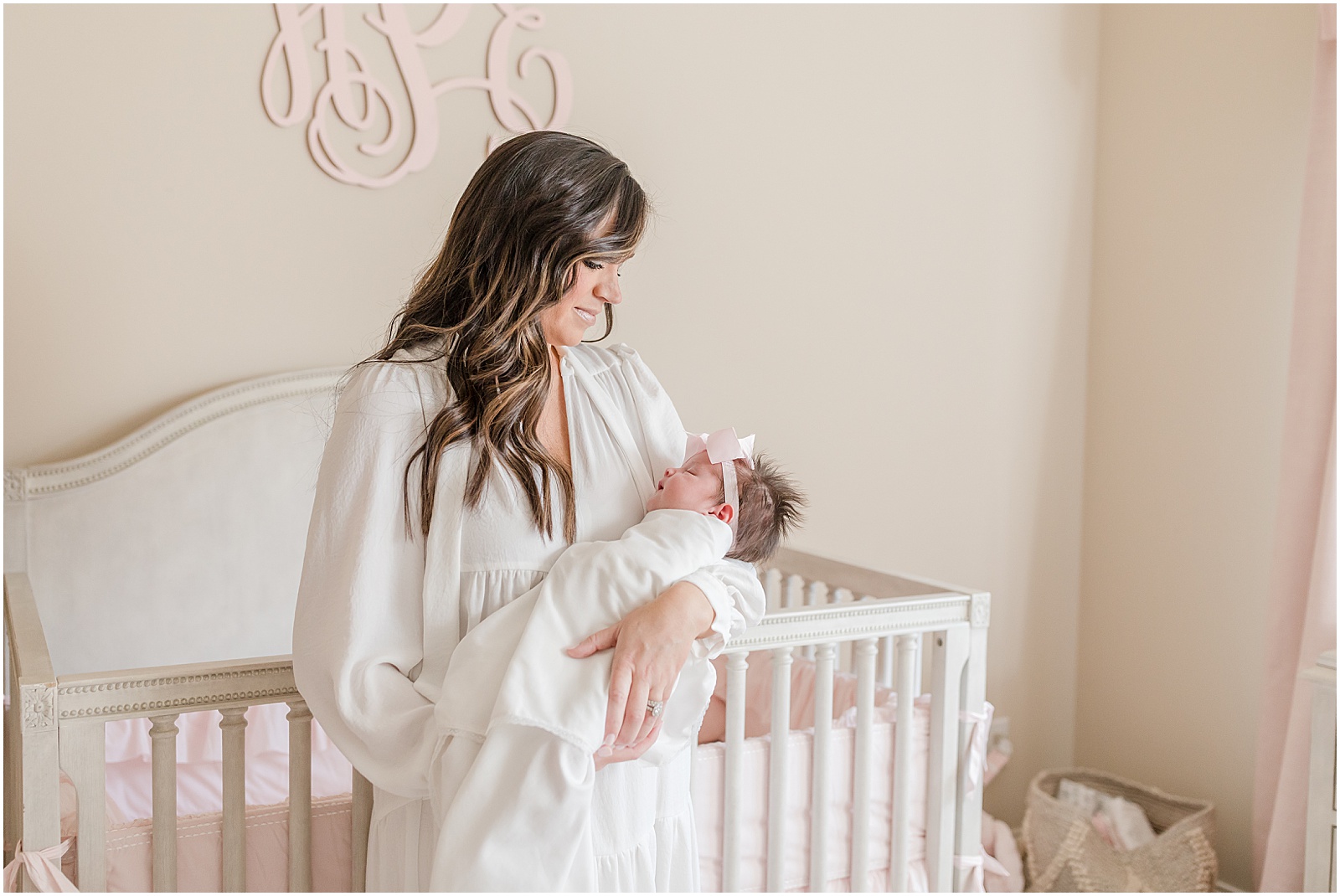 Portrait of mother gazing down at newborn baby standing in front of a white crib by Greenville photographer Molly Hensley