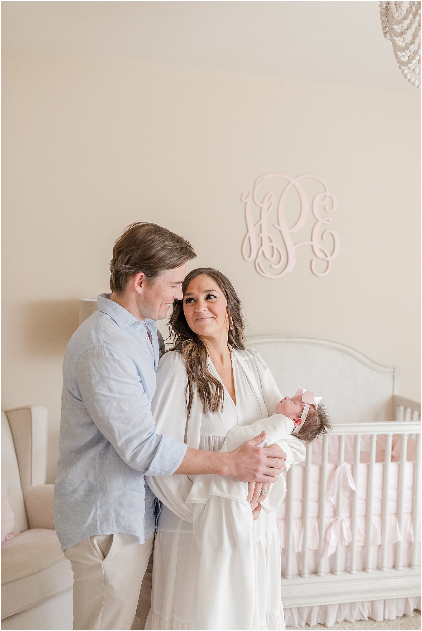 Portrait of parents holding newborn baby standing in front of a white crib by Greenville photographer Molly Hensley