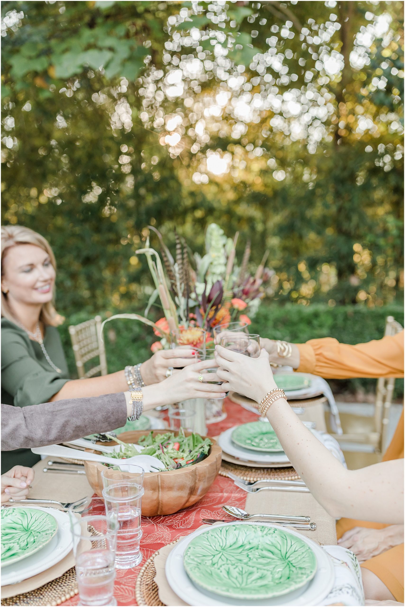 The hands of four women extending over a fall tabletop to cheers the meal.