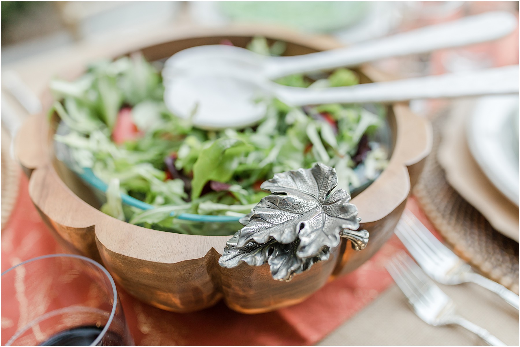 Close up of a serving salad bown that is wooden with a metal leaf embellishment.