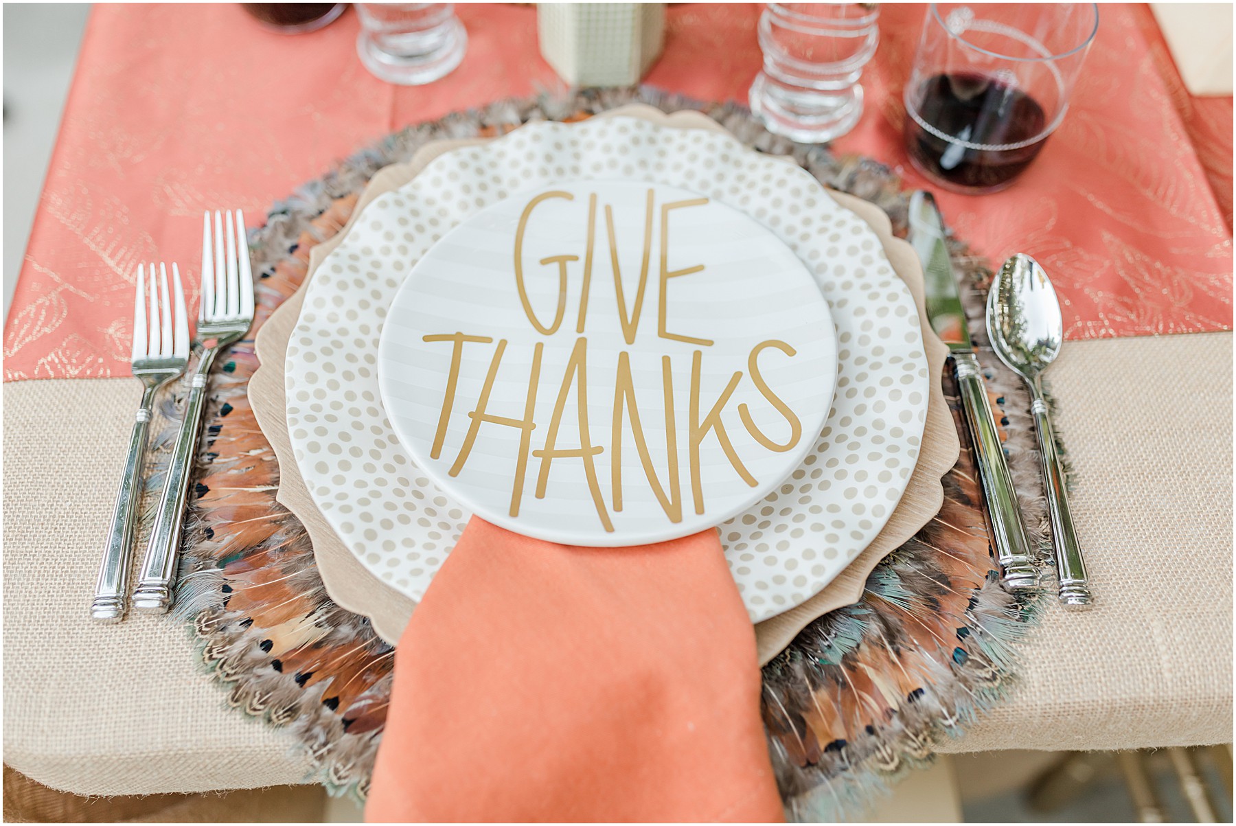 A thanksgiving table setting featuring a feather placemat and a plate that says "Give Thanks"