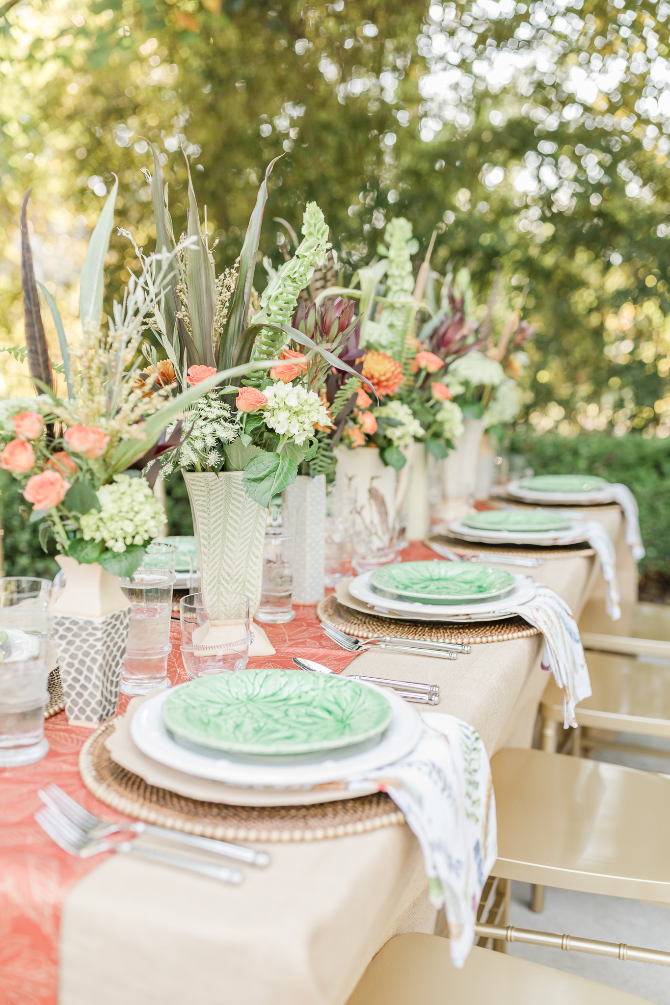 A fall table featuring china with green plates and a row of vases holding fall flowers.