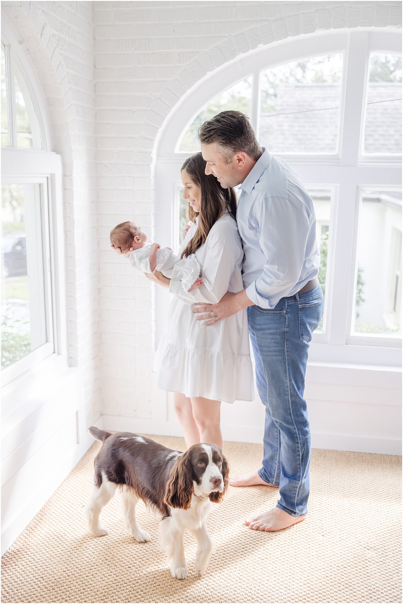 Mother and father looking at their baby while their dog stands at their feet for their Greenville newborn photo session.