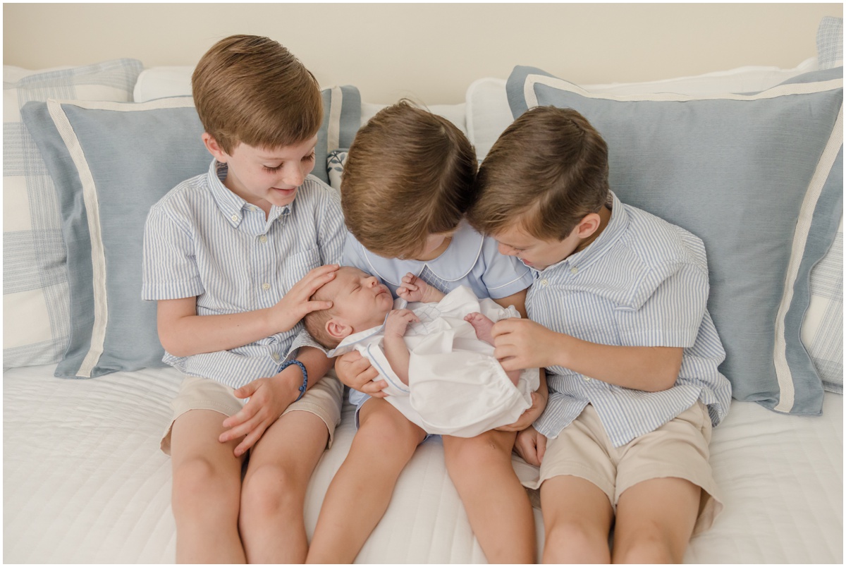 Greenville Newborn Photography of three young boys in blue holding their newborn baby brother.