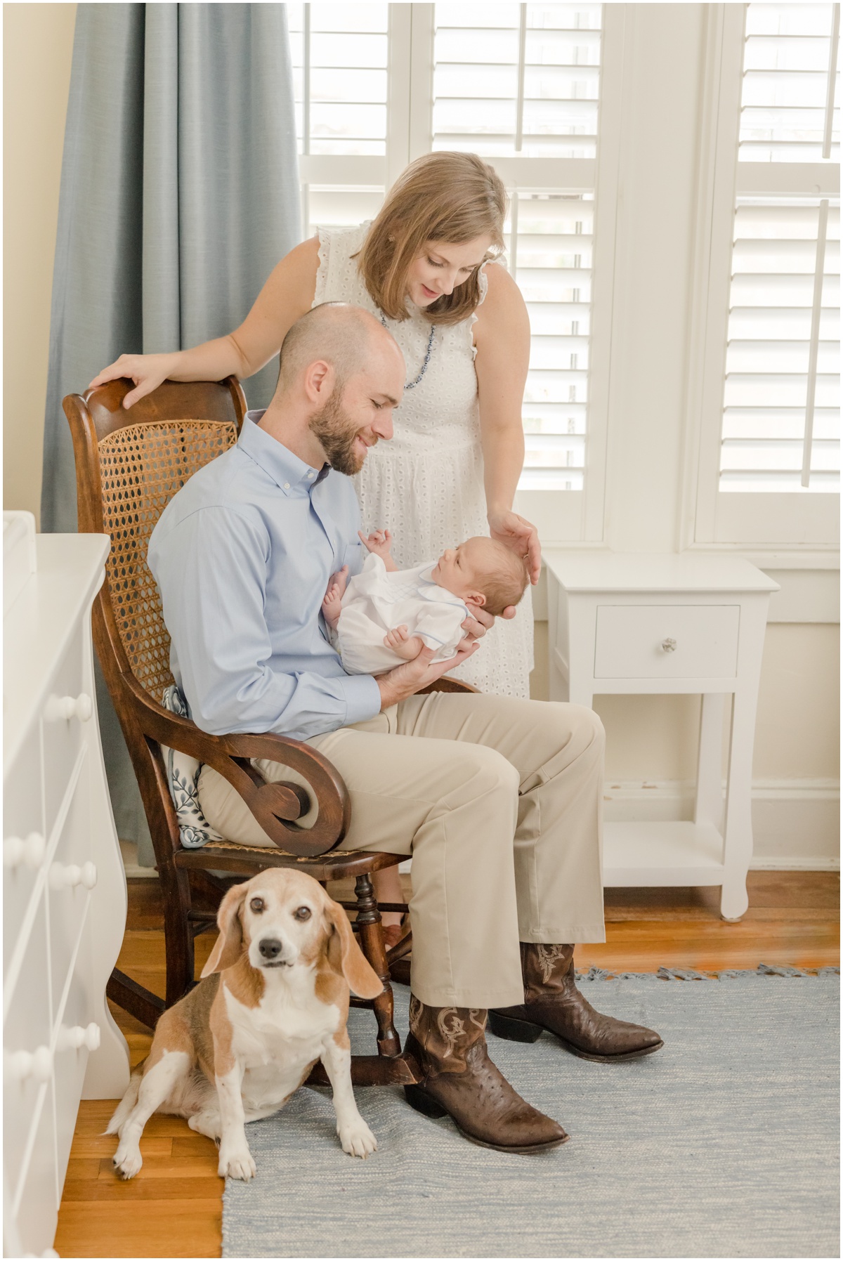 Greenville Newborn Photography of a father holding his newborn son in a rocking chair with his wife beside him while his beagle sits at his feet.