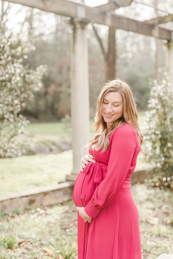 Portraits of a pregnant woman cradling belly in red dress by Greenville Maternity Photographer