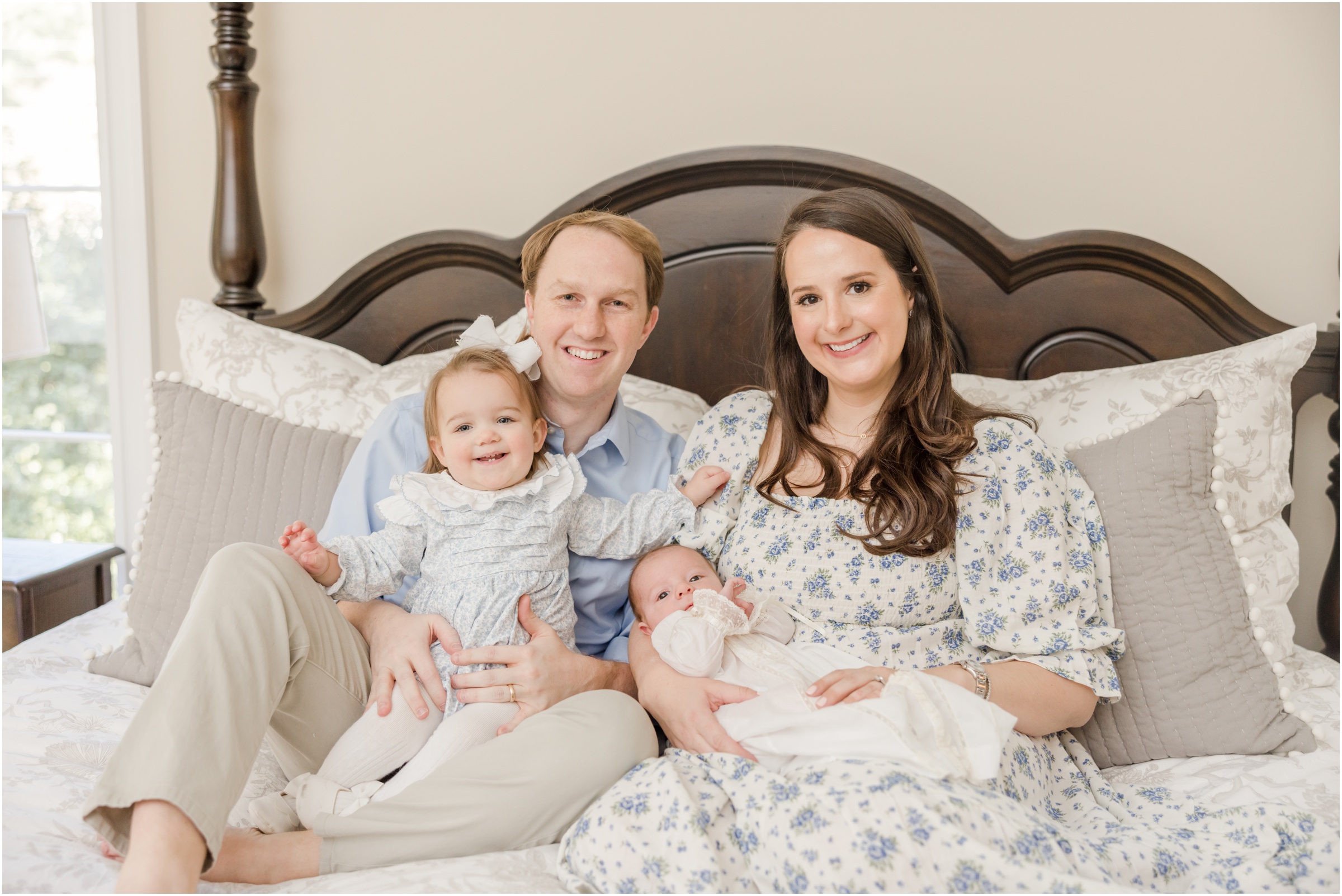 Portrait of two parents, their toddler daughter, and newborn son sitting on their bed during their Greenville newborn photography session.