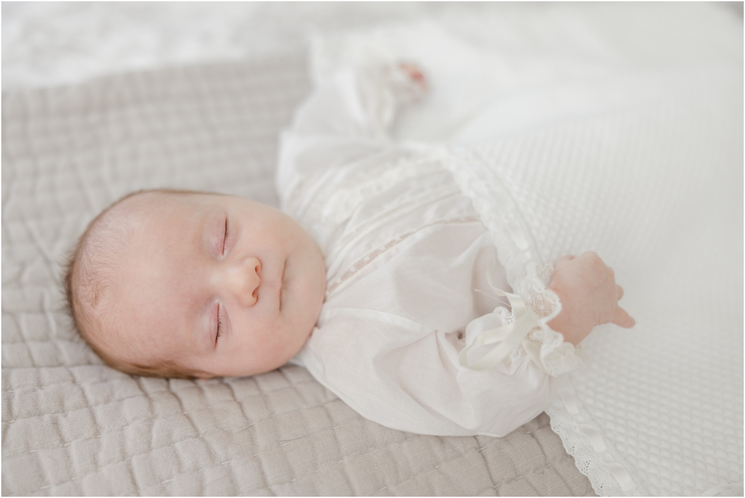 A newborn boy wearing a white lace heirloom gown covered by a white blanket for his Greenville newborn portrait.