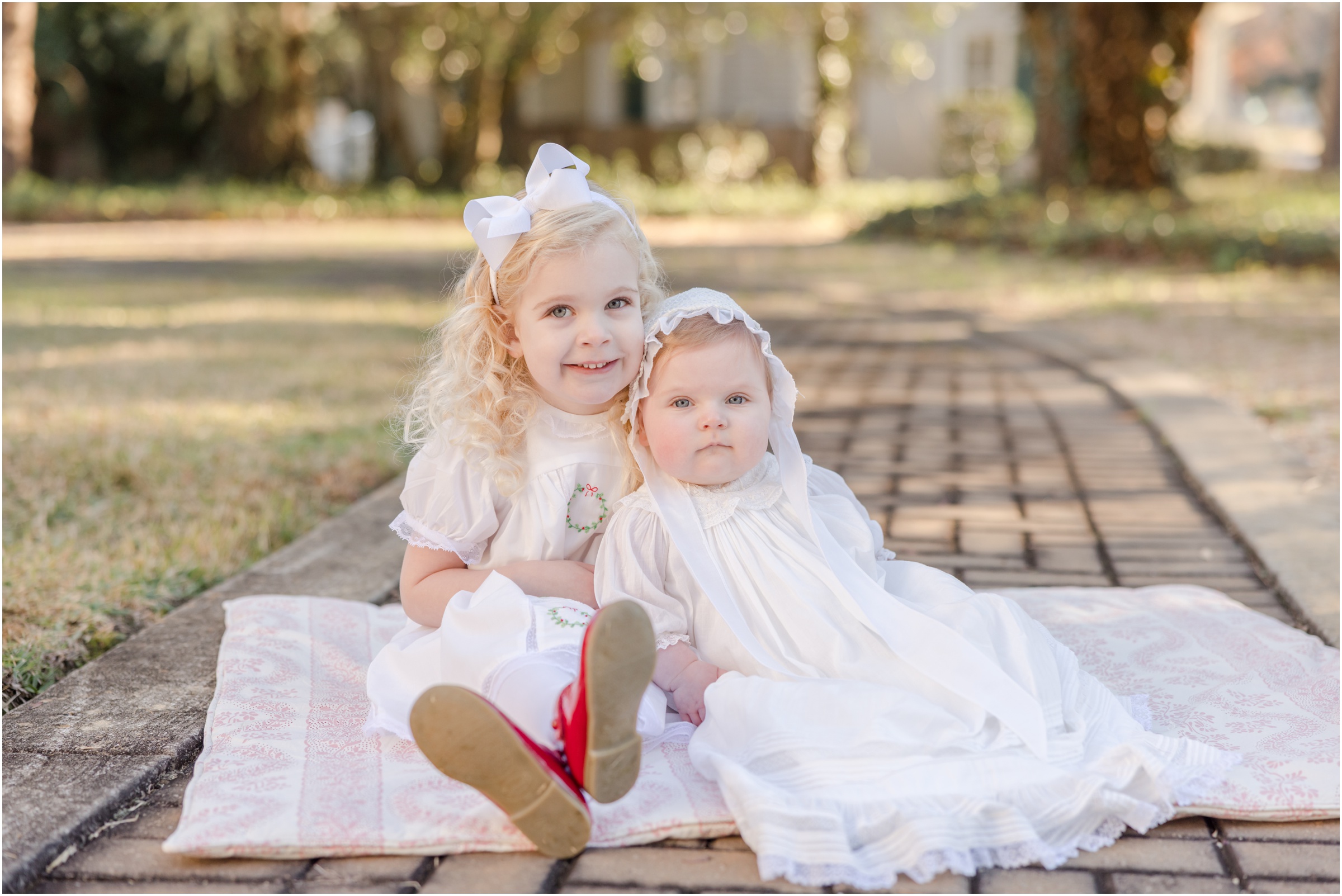 Young sisters sitting on a blanket on a stone path smiling for a portrait by Greenville SC family photographer Molly Hensley.
