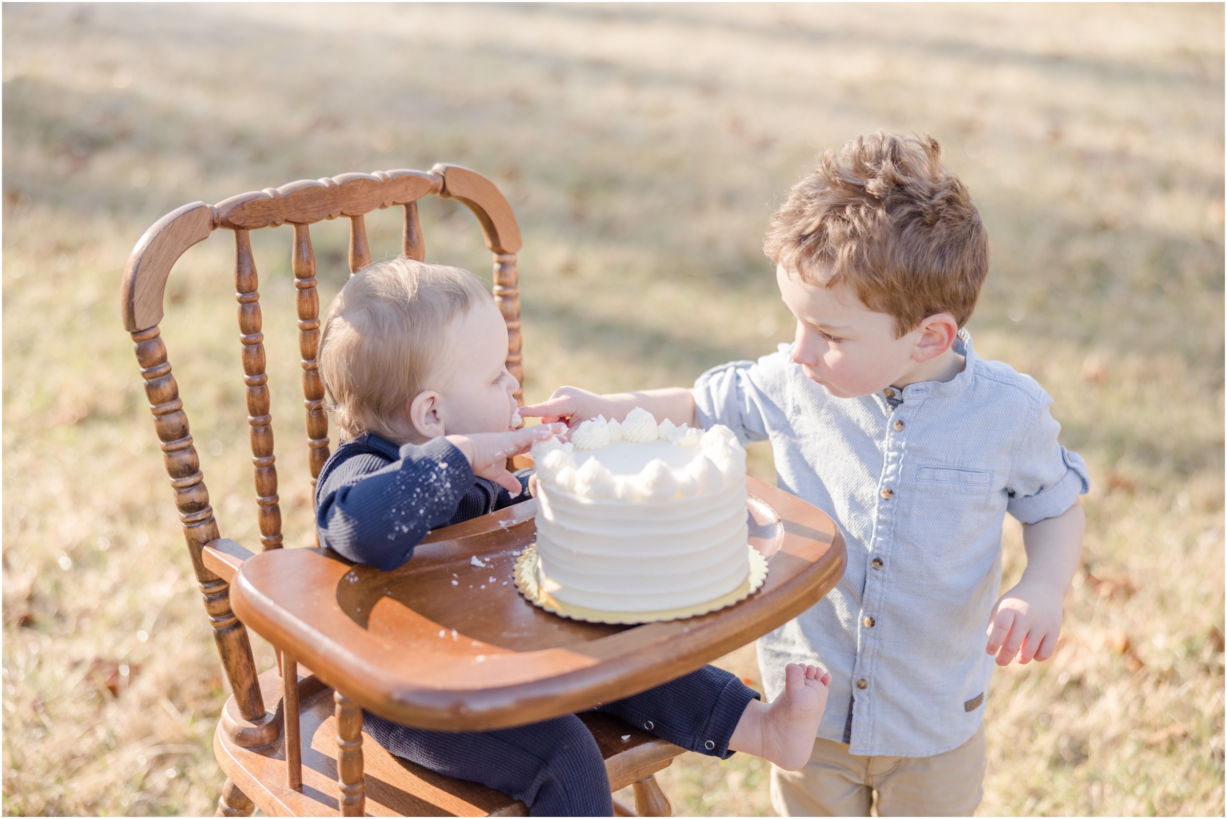 A three year old boy extends his icing covered finger to his baby brother during cake smash photos in Greenville.