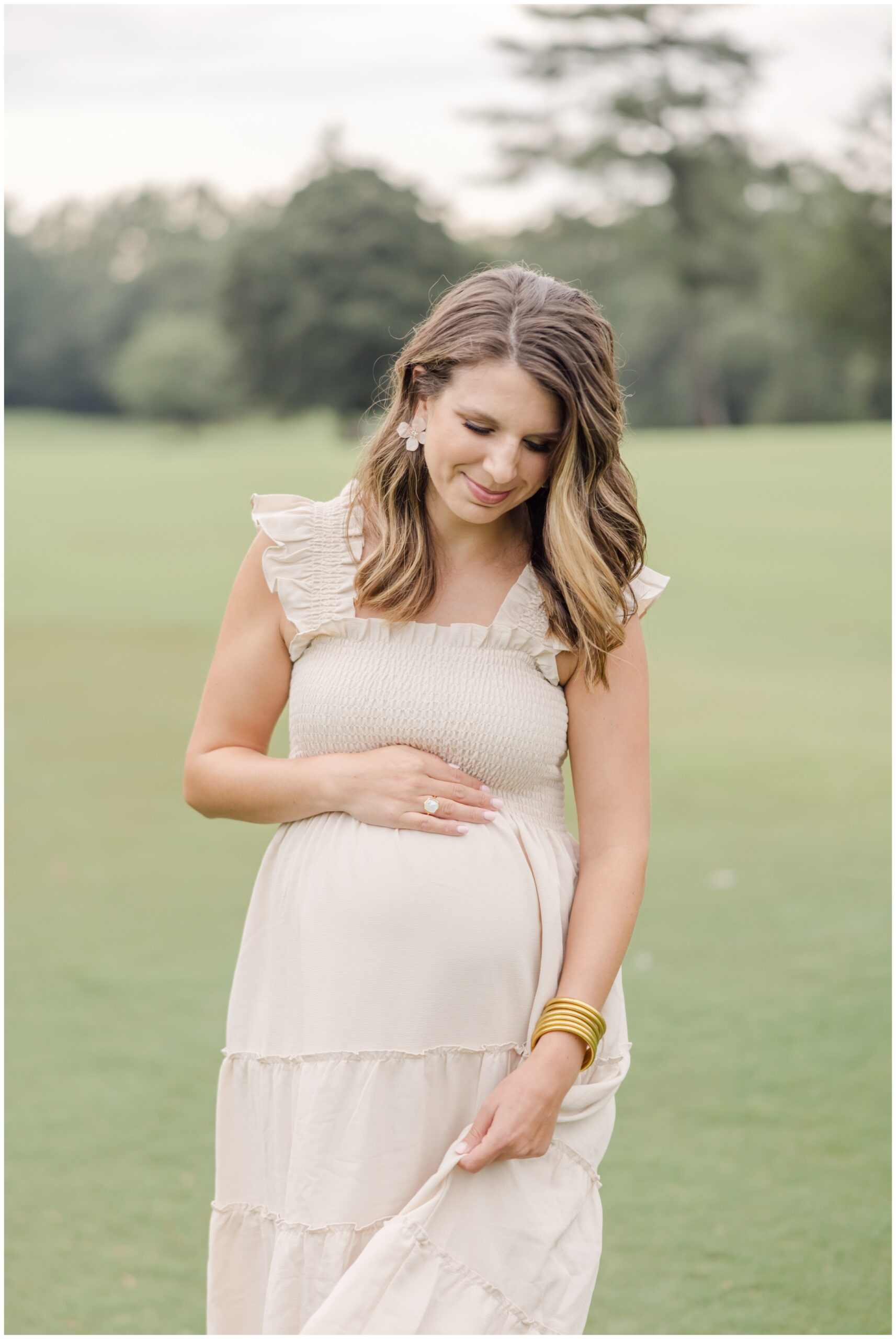 Pregnant mother smiling softly while cradling her baby bump during Greenville SC maternity photos.