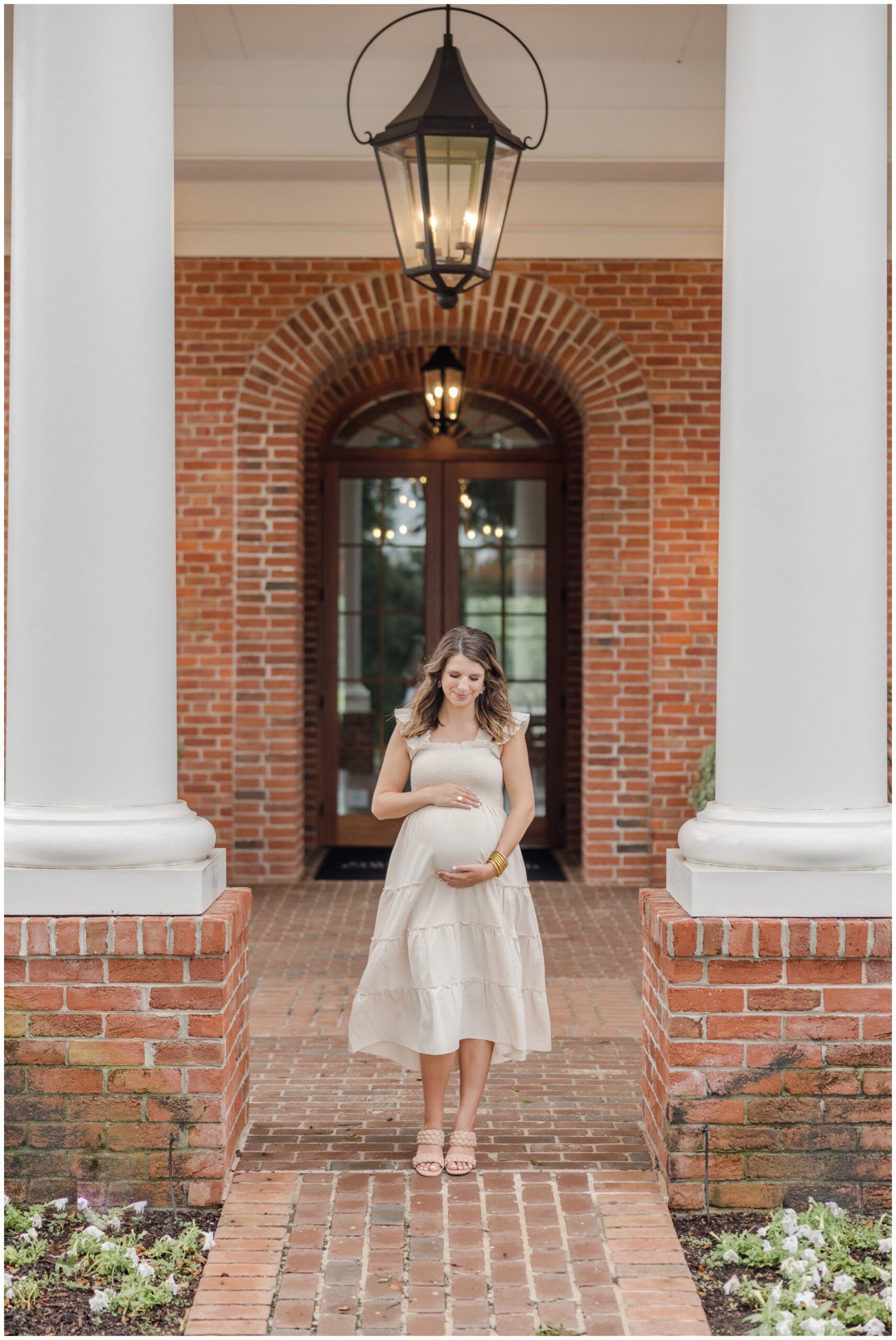 Expecting mother cradling her belly framed between arches in front of a brick building.