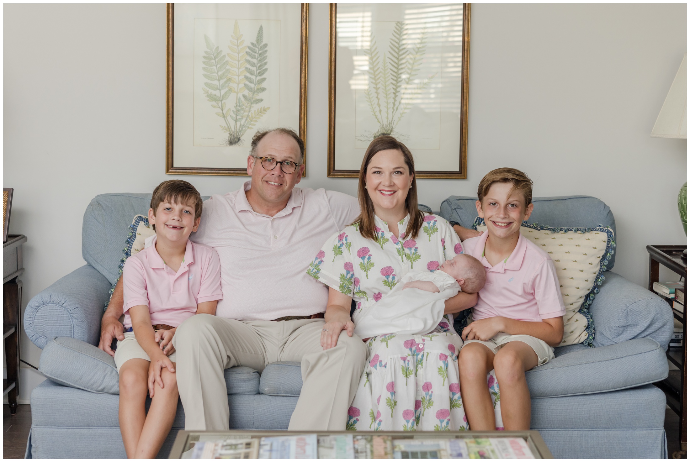 A family seated on a couch posing for a photo during their Greenville in Home newborn session.