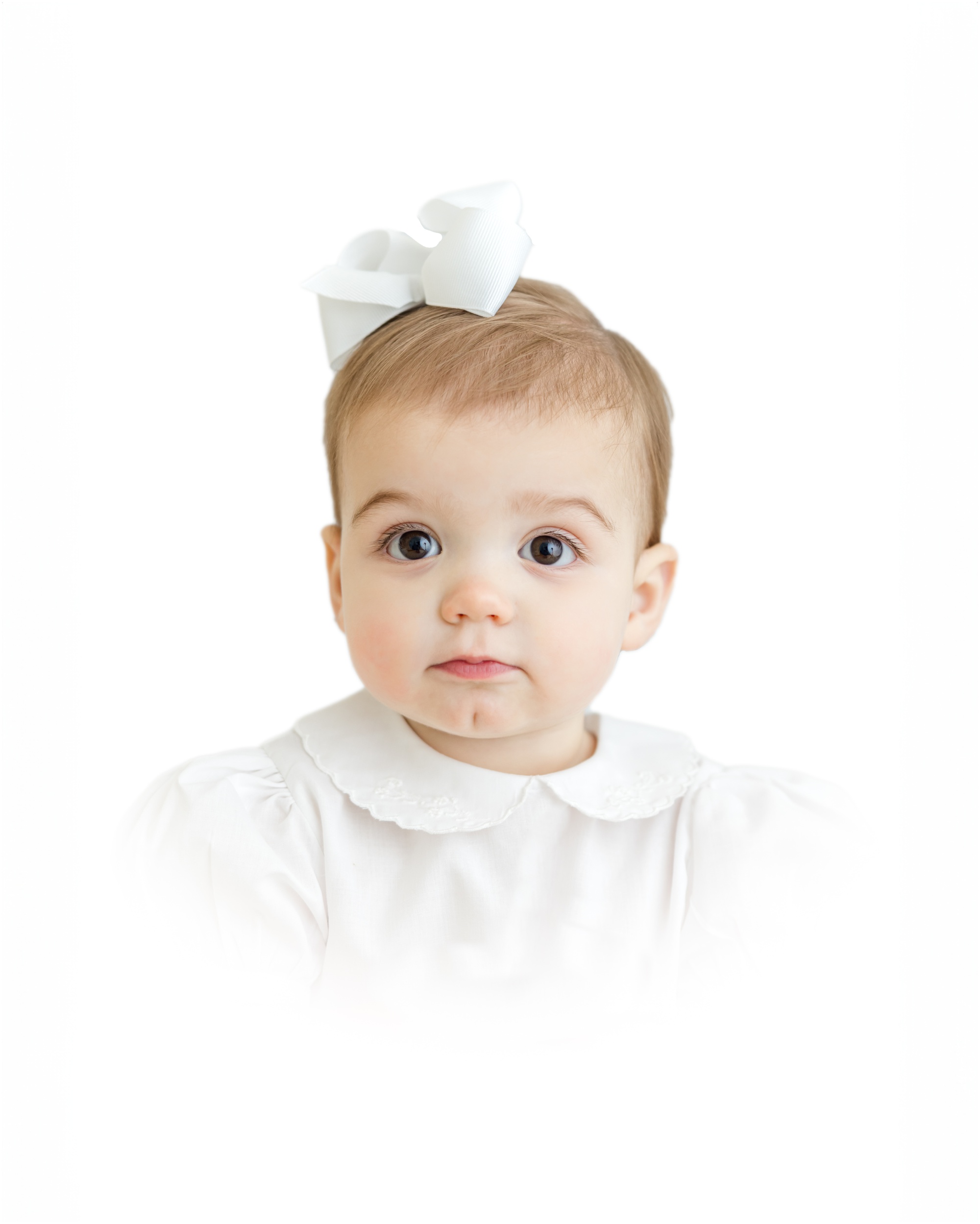 A traditional heirloom portrait of a one year old girl with a serious expression in white with a white bow with a white vignette by Greenville photographer Molly Hensley.