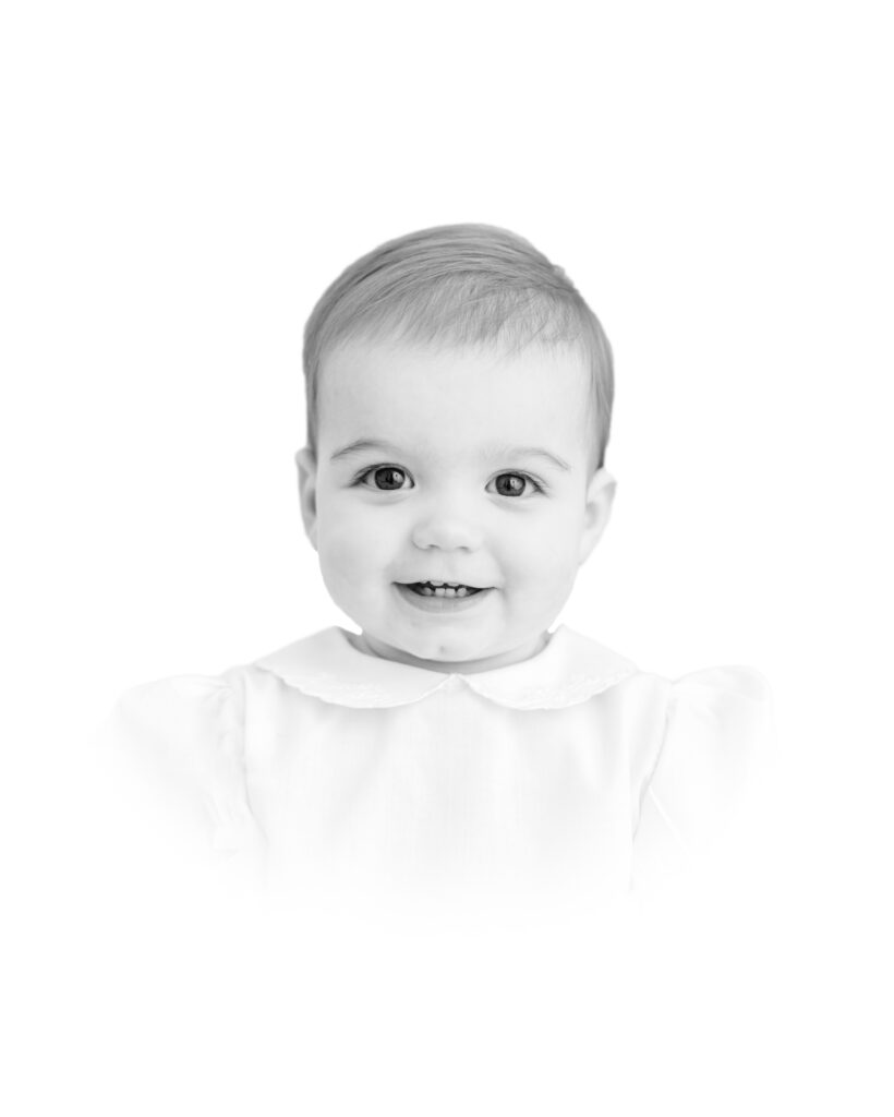 A black and white traditional heirloom portrait of a smiling one year old girl with a white vignette by Greenville photographer Molly Hensley.