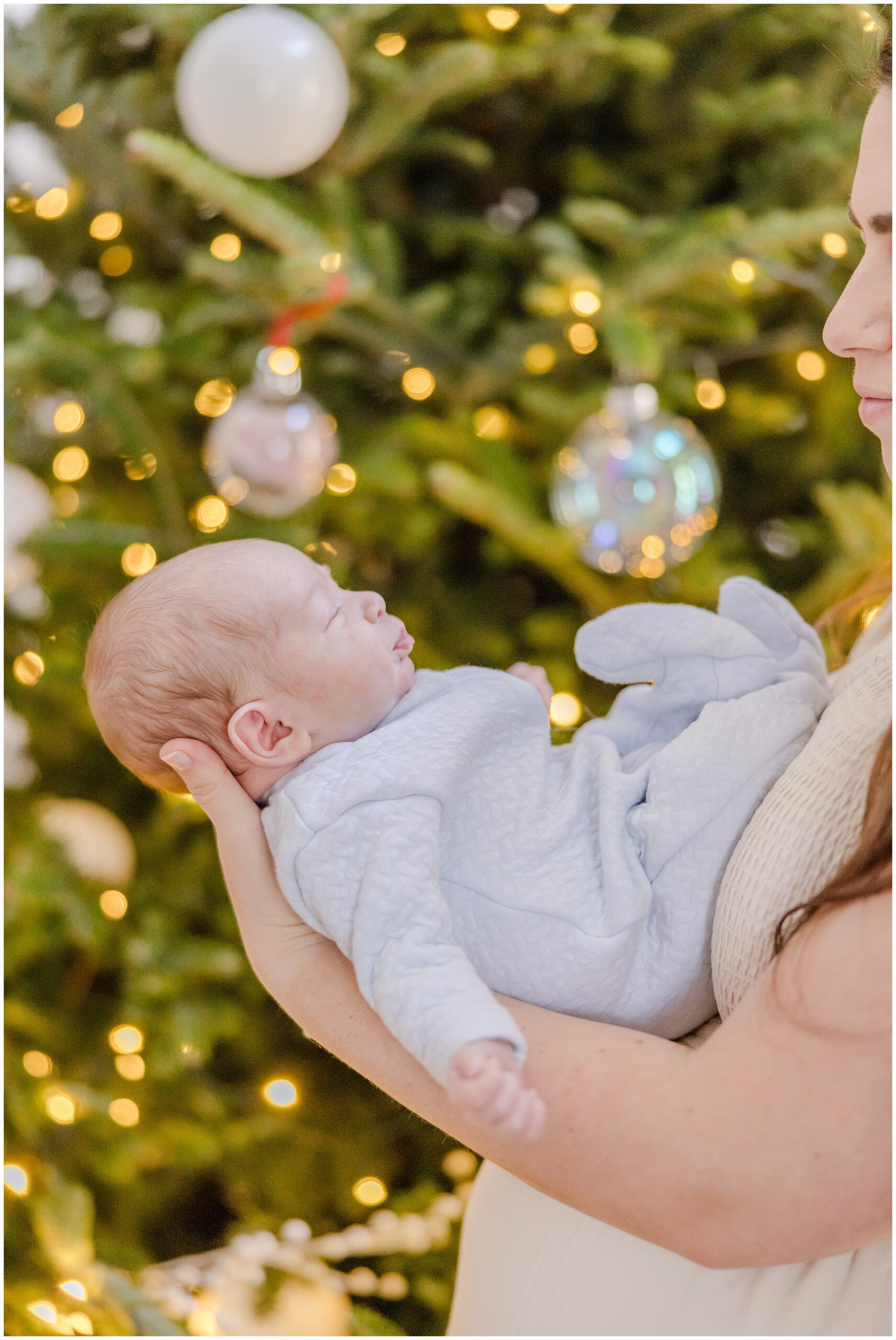 A portrait of a newborn baby boy being held in front of a christmas tree with glowing lights.